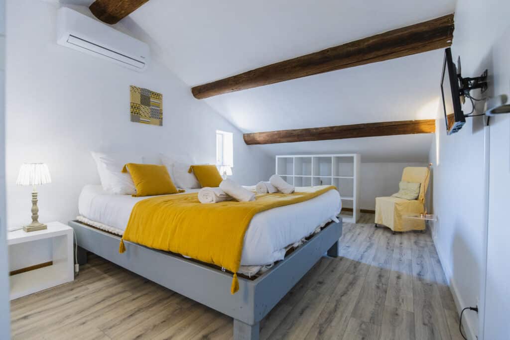 Chambre sous les poutres avec lit double à plaid jaune, climatisation et meuble de rangement