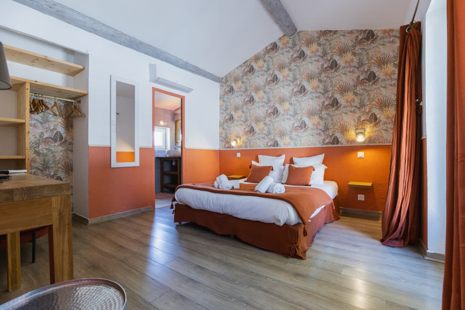 Chambre avec lit double, murs terracotta, papier peint feuillage tropical et poutres apparentes