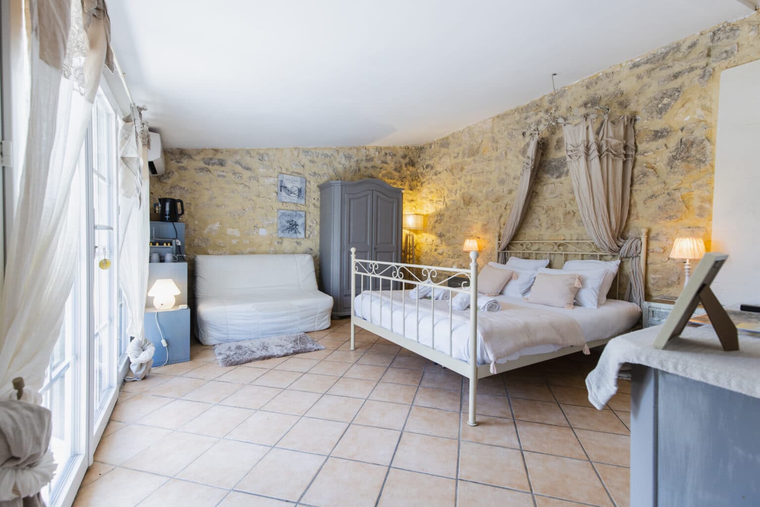 Chambre en pierre apparente avec lit à baldaquin, lit simple et canapé blanc, sous un plafond bas