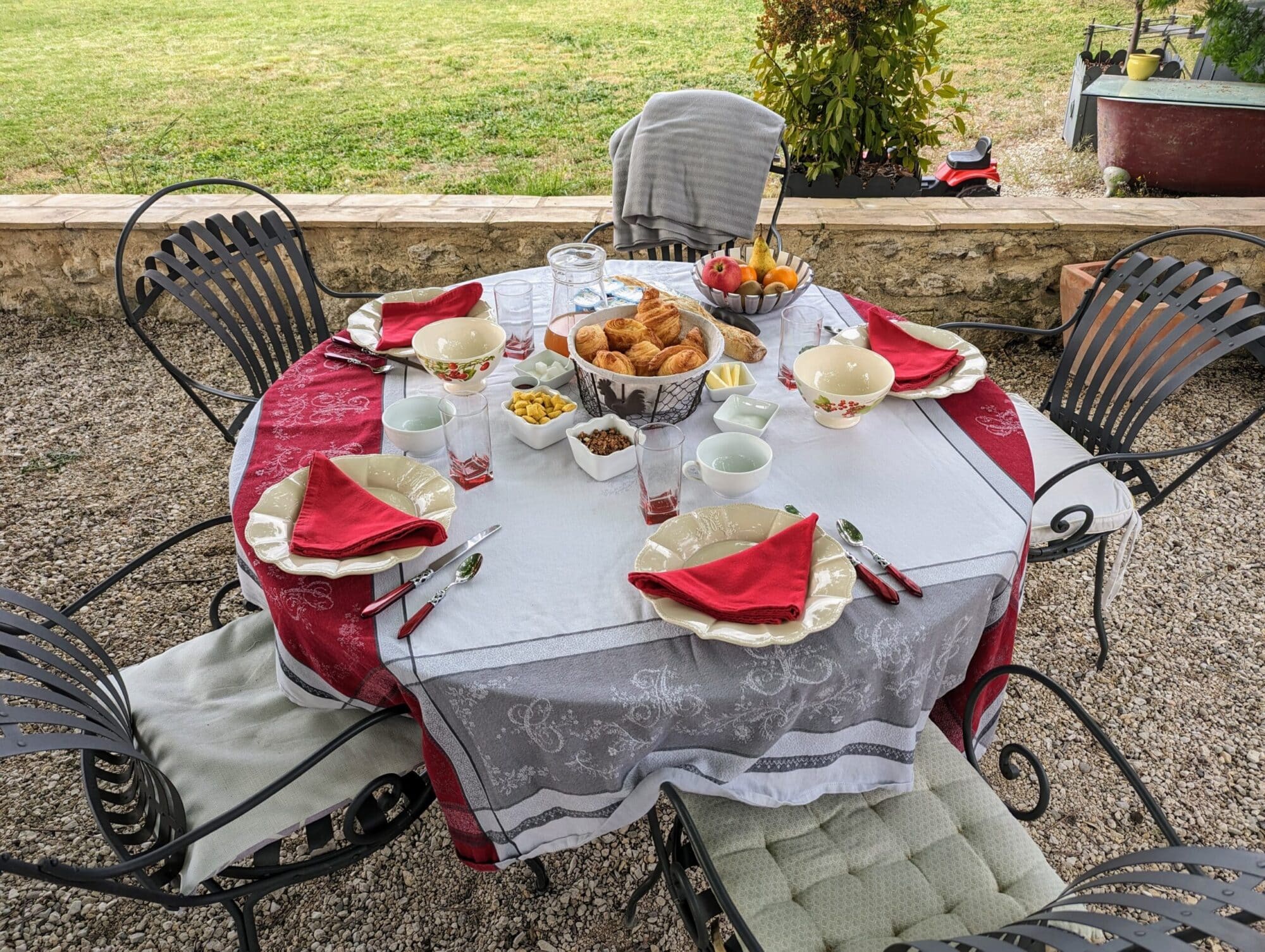 Table de petit-déjeuner garnie de viennoiseries, fruits et boissons, sous les arbres du jardin, avec vue sur la campagne