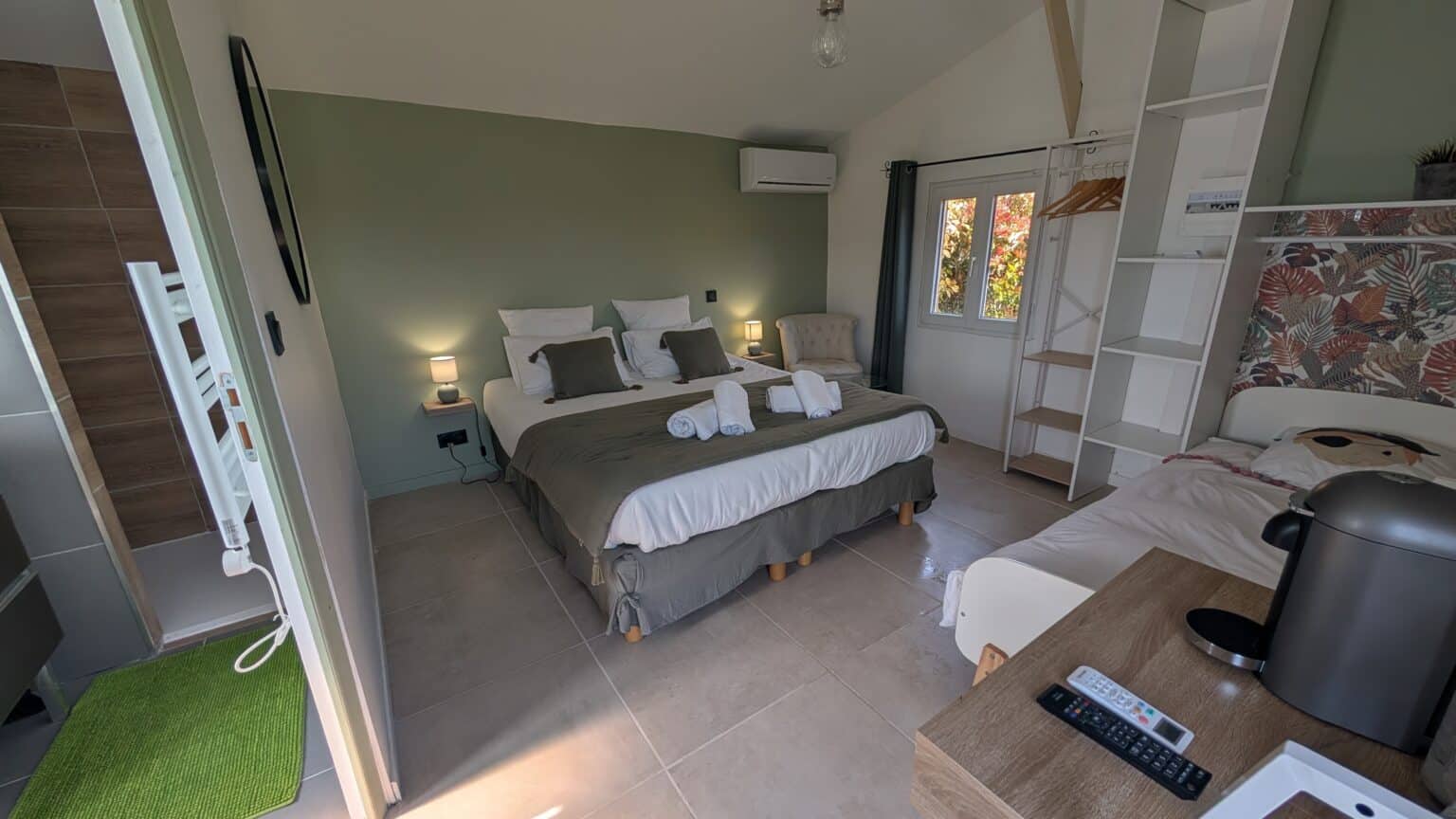 Chambre familiale avec lit double, mur vert sauge, lit simple d’appoint, dressing ouvert, climatisation et salle d’eau attenante